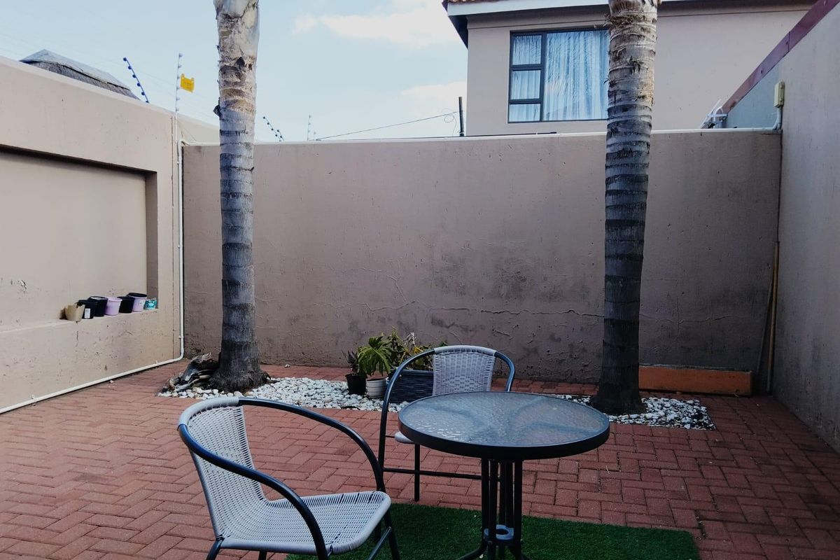 A private rear courtyard featuring paved flooring, boundary walls with electric fencing, and established palm trees, offering a low-maintenance outdoor space.