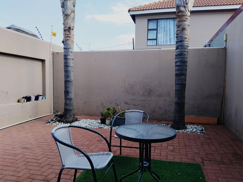 A private rear courtyard featuring paved flooring, boundary walls with electric fencing, and established palm trees, offering a low-maintenance outdoor space.
