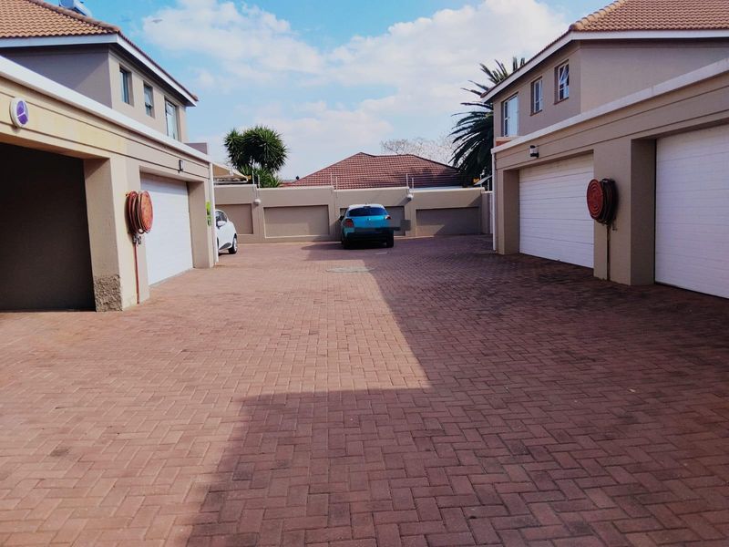 A paved communal driveway area featuring multiple sectional garage doors and perimeter walling for a townhouse complex.