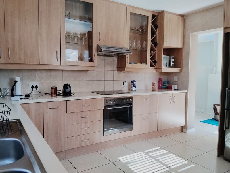 A functional kitchen featuring light wood cabinetry, integrated appliances including an oven and hob, tiled backsplash, and durable ceramic floor tiles.