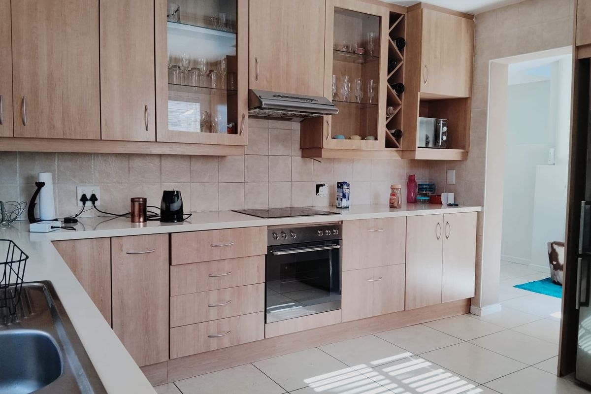A functional kitchen featuring light wood cabinetry, integrated appliances including an oven and hob, tiled backsplash, and durable ceramic floor tiles.