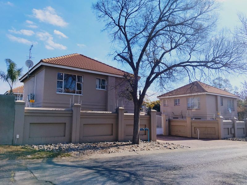 Front exterior view of a townhouse complex featuring a perimeter wall with electric fencing, tiled roofing, and a paved driveway.