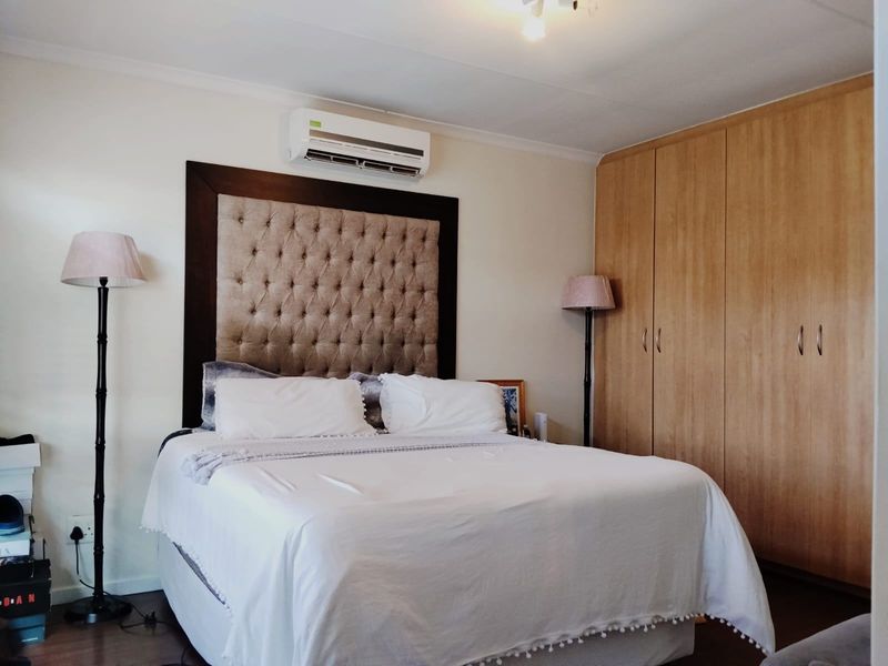 A well-maintained bedroom featuring built-in wooden cupboards, laminate flooring, and a wall-mounted air conditioning unit.