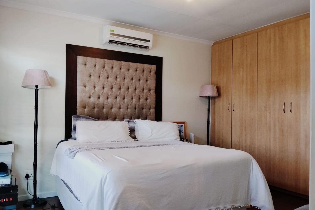 A well-maintained bedroom featuring built-in wooden cupboards, laminate flooring, and a wall-mounted air conditioning unit.