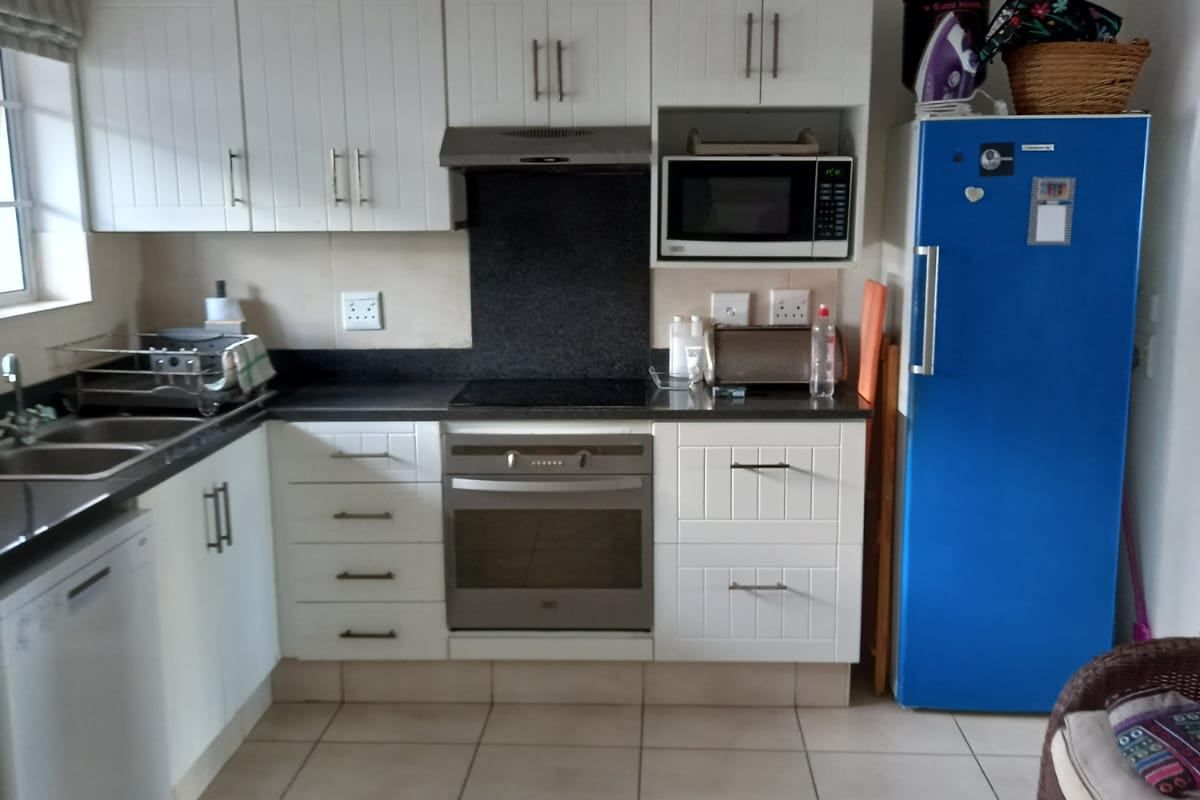 A functional kitchen featuring white cabinetry, dark countertops, built-in oven and hob, and tiled flooring, offering a clean and practical workspace.