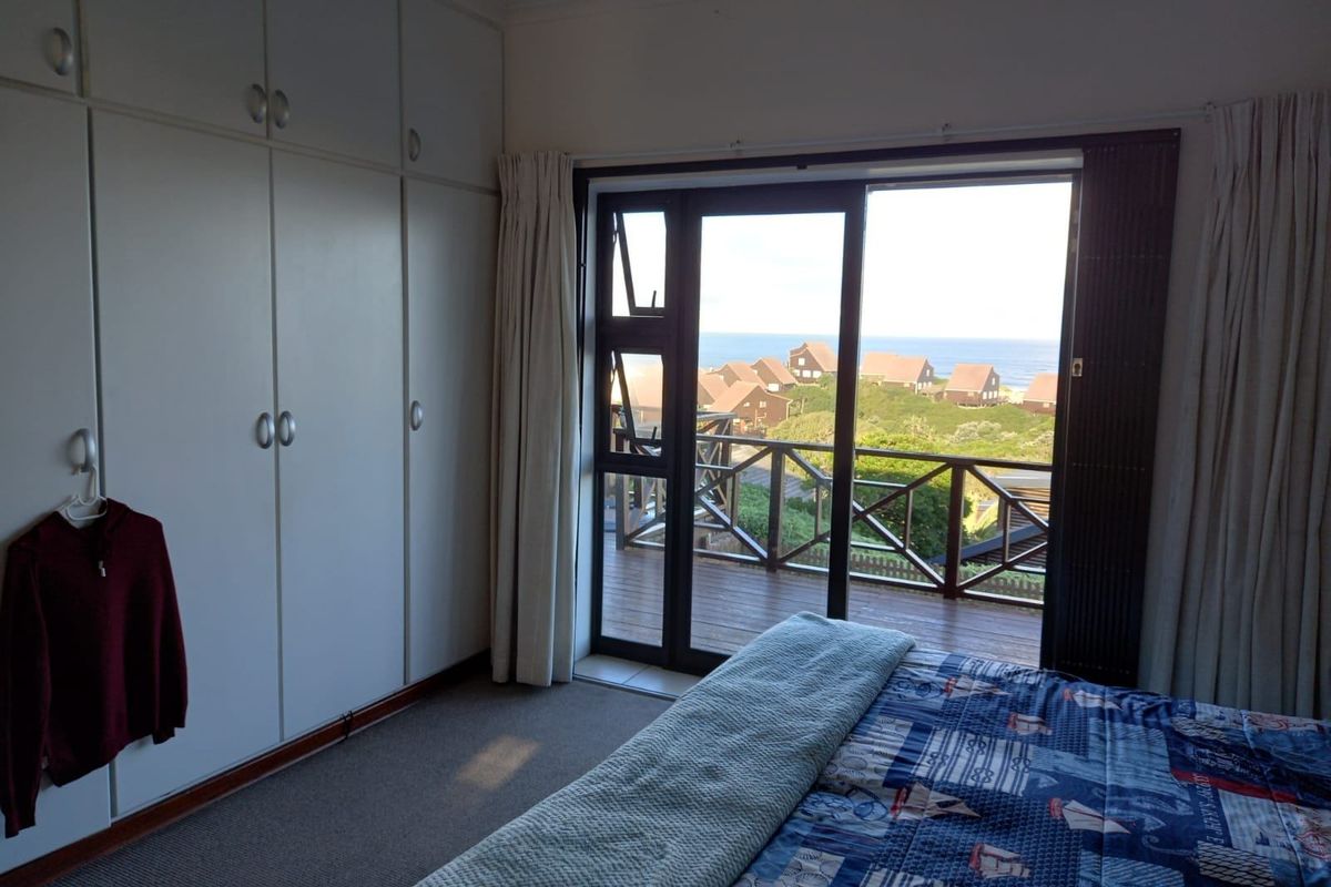 Bedroom featuring built-in cupboards, carpeted flooring, and a sliding glass door opening onto a balcony with scenic coastal views.