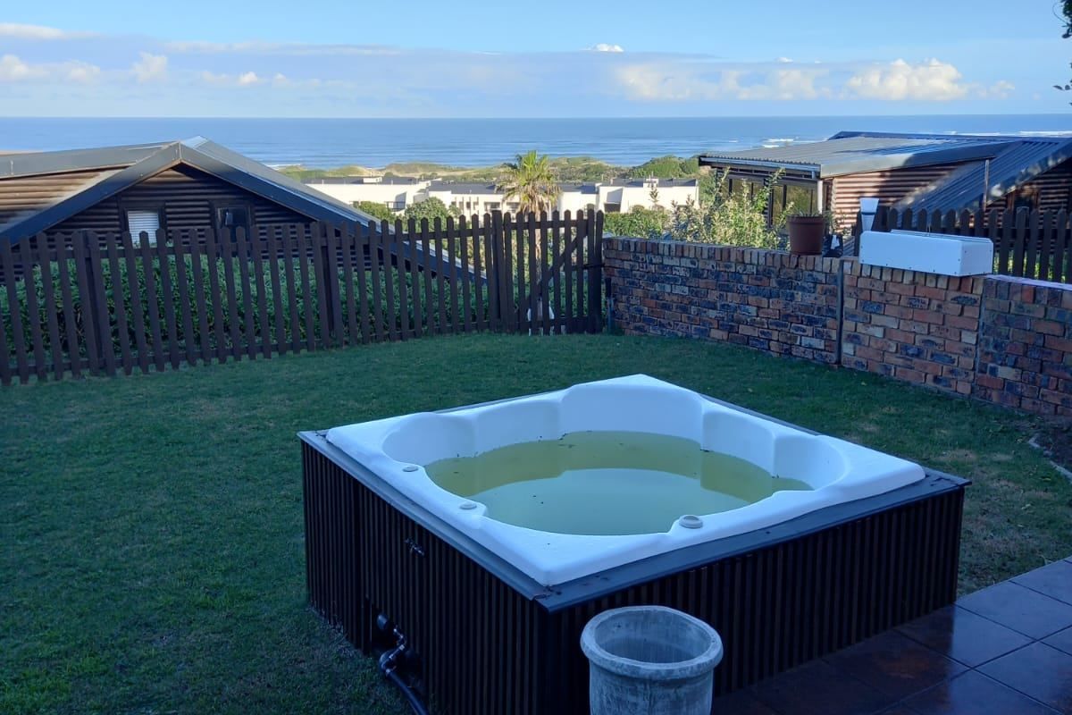 Rear garden area featuring a built-in jacuzzi, tiled patio, and brick boundary wall with scenic ocean views.