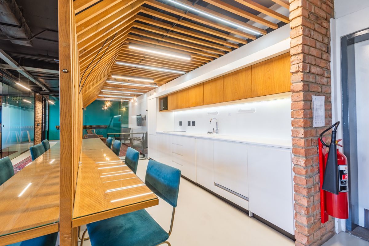 Modern commercial kitchen area featuring sleek white cabinetry, timber slat ceiling details, and an exposed brick accent wall with integrated lighting.