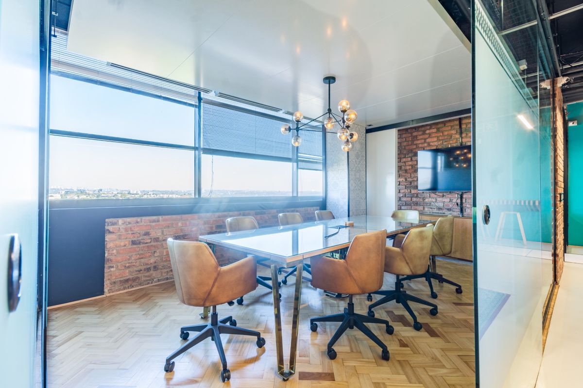 Modern professional boardroom featuring herringbone parquet flooring, exposed brick accents, and large windows providing ample natural light and city views.