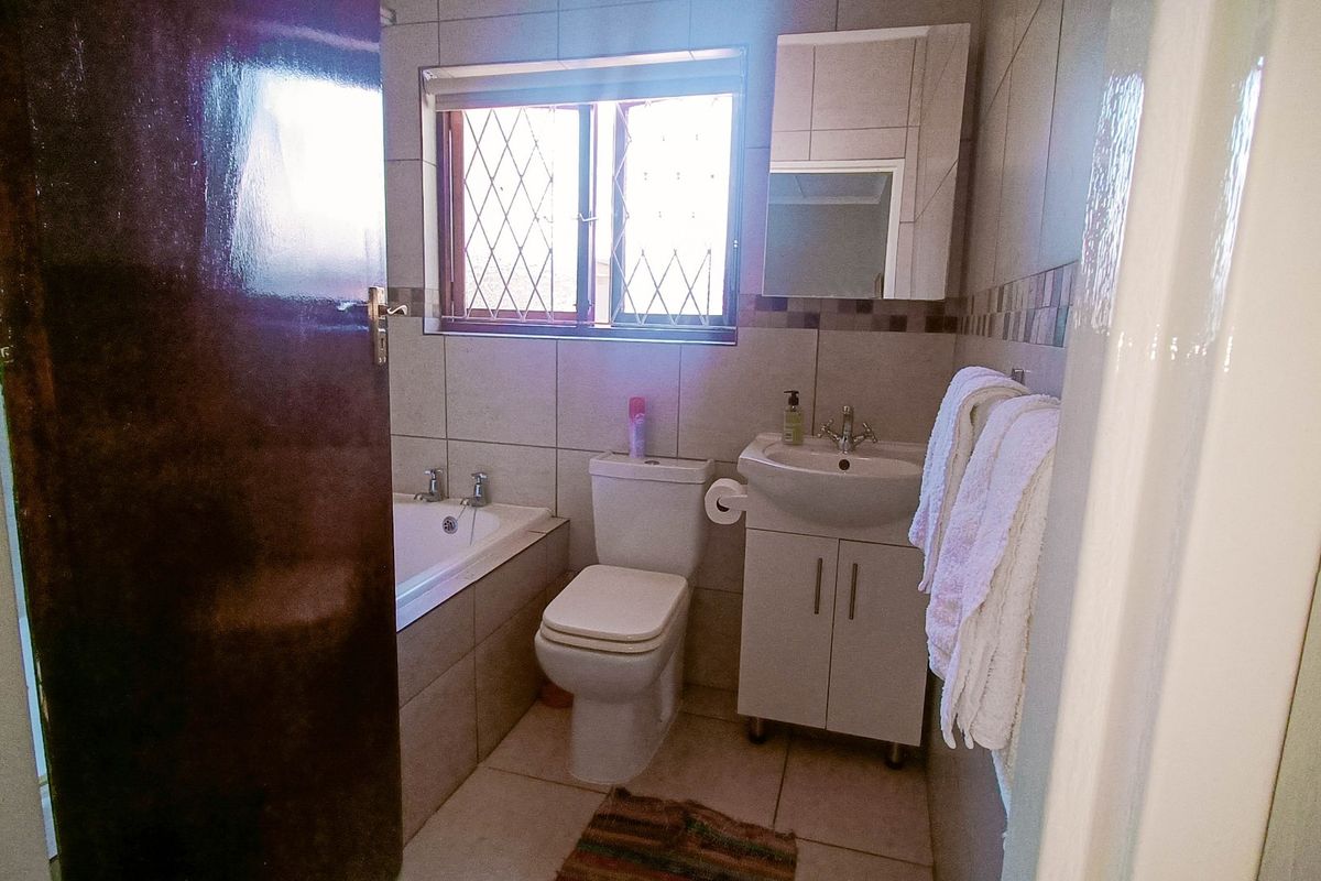 A functional bathroom featuring a built-in bathtub, toilet, vanity cabinet with washbasin, and tiled finishes throughout.