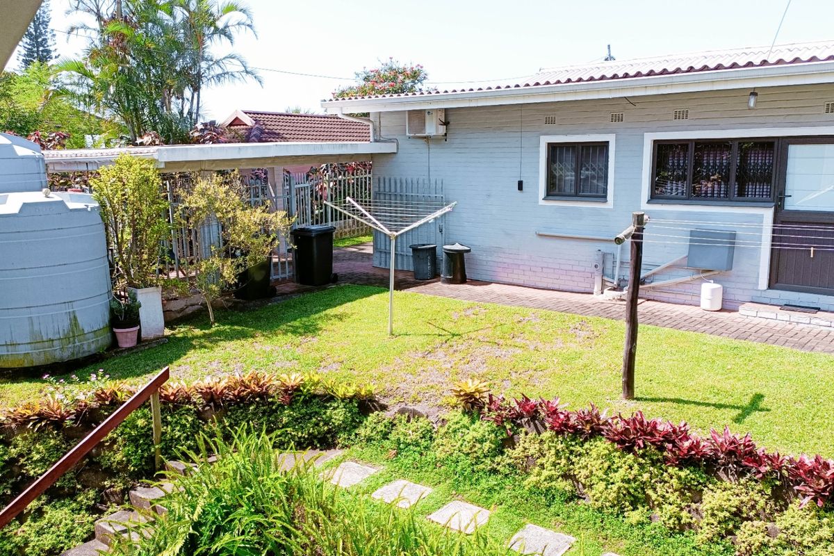 Rear exterior view of the apartment featuring a private garden, paved patio area, water storage tank, and secure perimeter fencing.