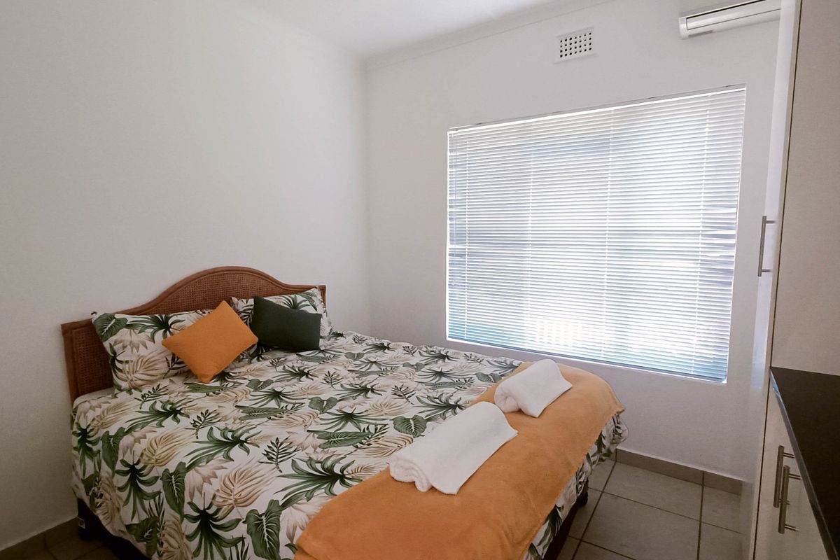 A clean and functional bedroom featuring tiled flooring, built-in storage, venetian blinds, and a wall-mounted air conditioning unit.