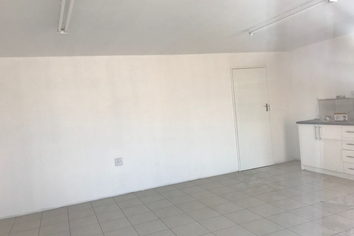 An open-plan industrial space featuring tiled flooring, fluorescent lighting, and a compact built-in kitchenette area.