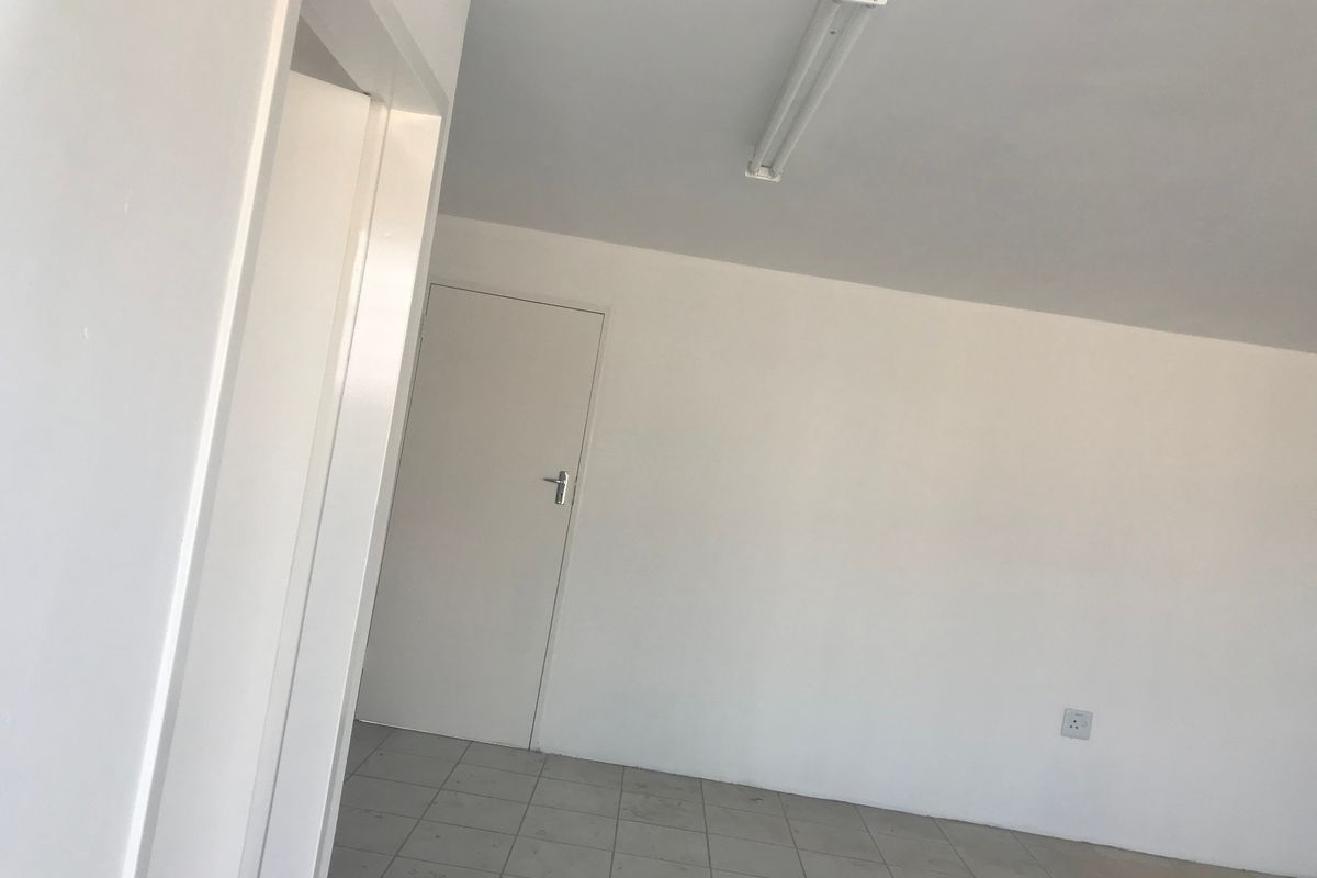 A clean, empty office space featuring neutral white walls, tiled flooring, and a functional overhead fluorescent light fixture.