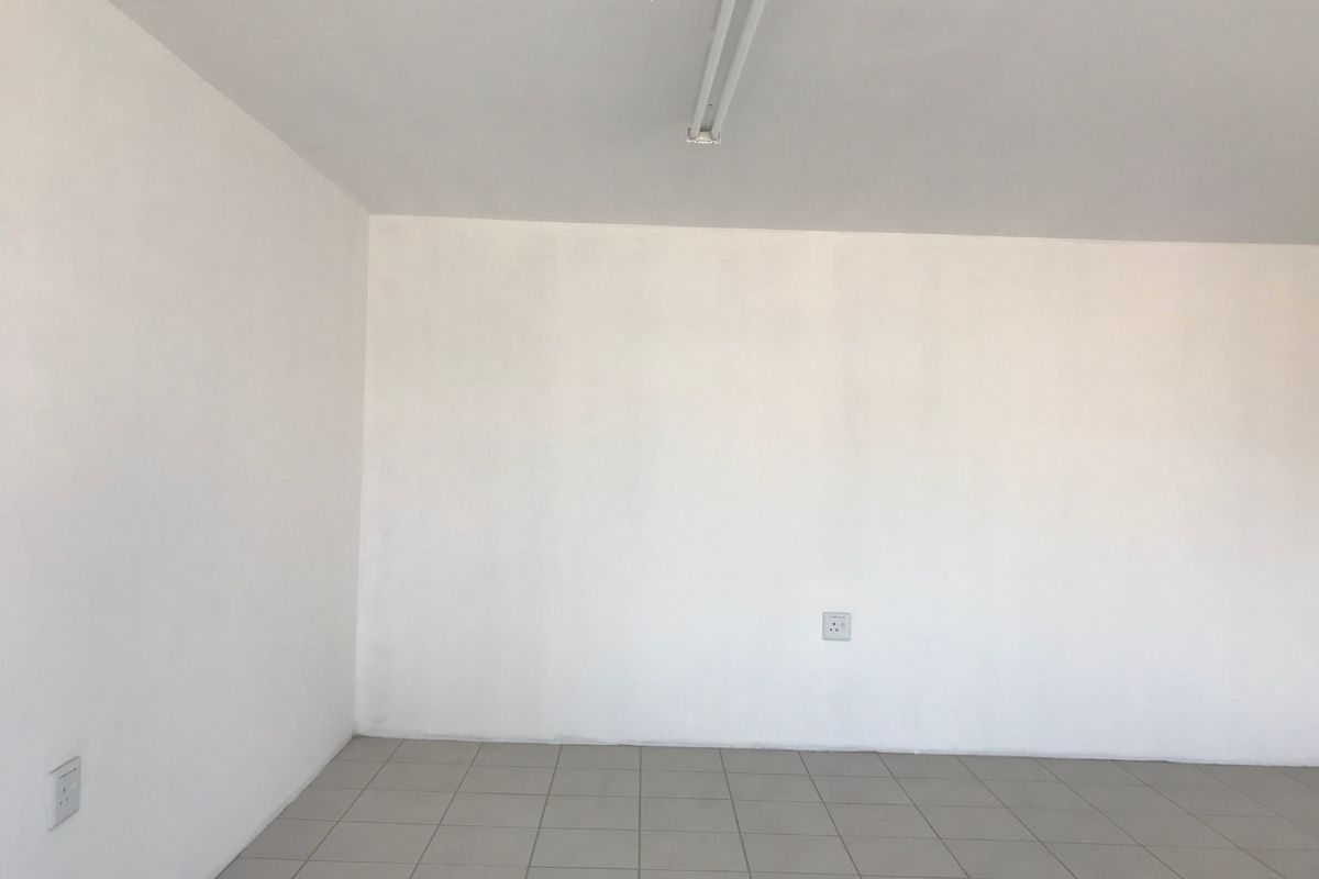 A clean, empty industrial utility space featuring neutral tiled flooring, white walls, and functional overhead strip lighting.