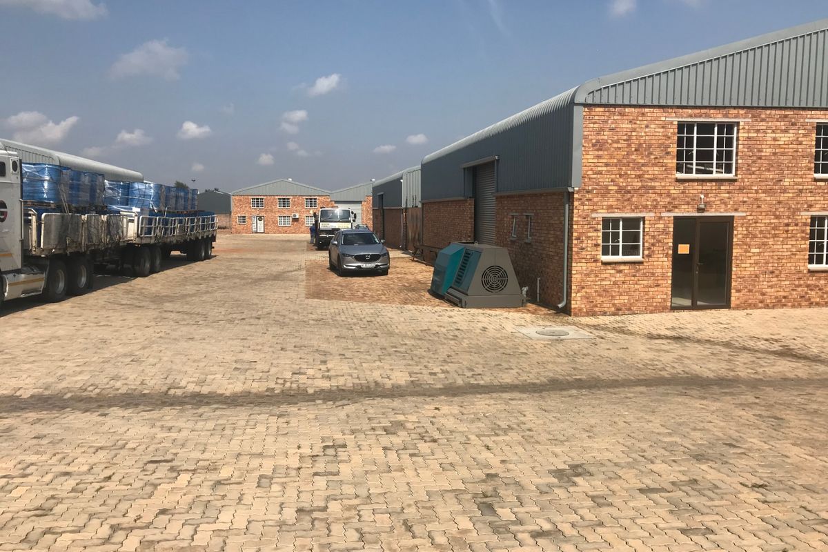 Industrial property exterior featuring brick warehouse buildings, metal roofing, and a large paved yard area suitable for logistics and heavy vehicle access.