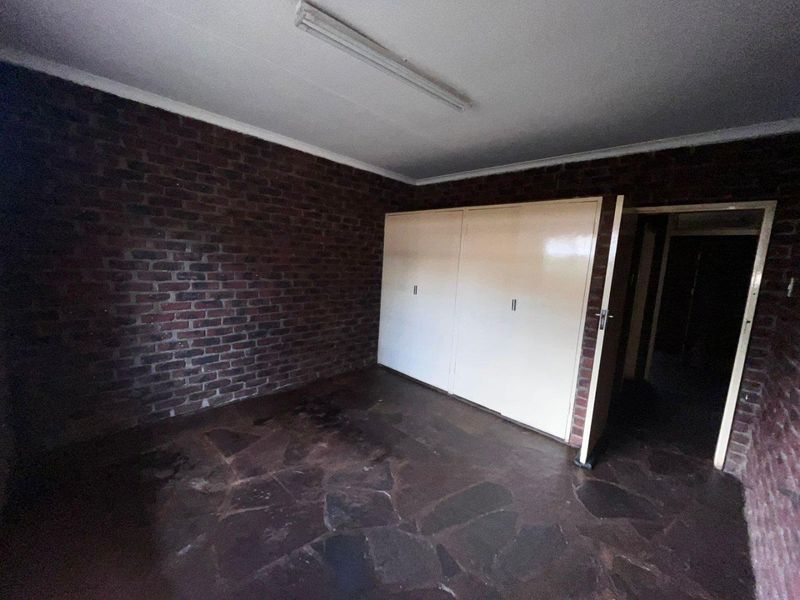 An empty bedroom featuring exposed brick walls, stone tile flooring, and built-in cupboards, offering a blank canvas for renovation.