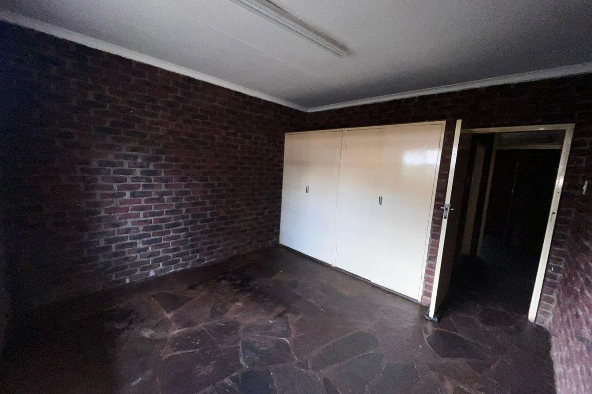 An empty bedroom featuring exposed brick walls, stone tile flooring, and built-in cupboards, offering a blank canvas for renovation.