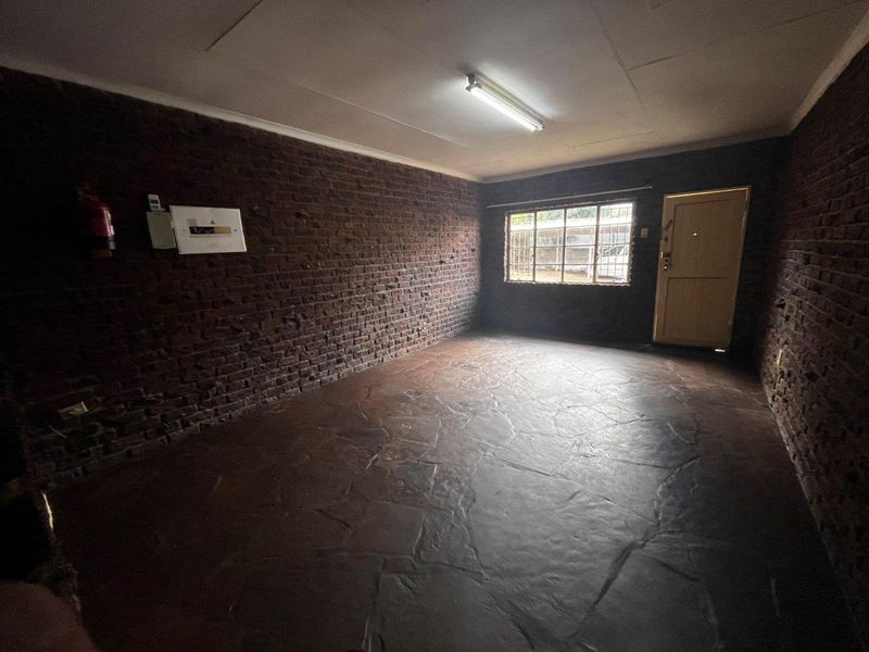 An empty living area featuring exposed brick walls, stone tile flooring, and a security gate, offering a blank canvas for renovation.
