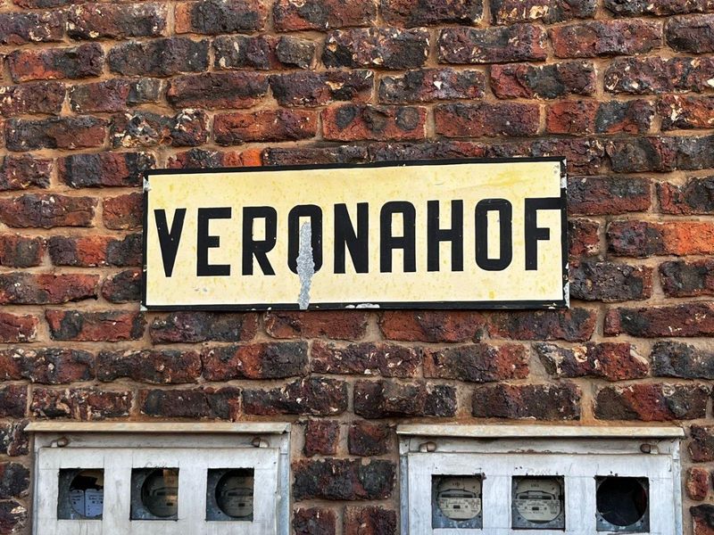 Close-up view of the Verona Hof building signage mounted on an exposed brick facade with integrated utility meter boxes.