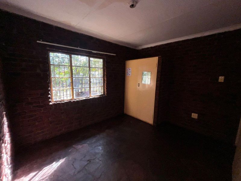 An empty bedroom featuring exposed brick walls, a window with security bars, and a simple interior door.