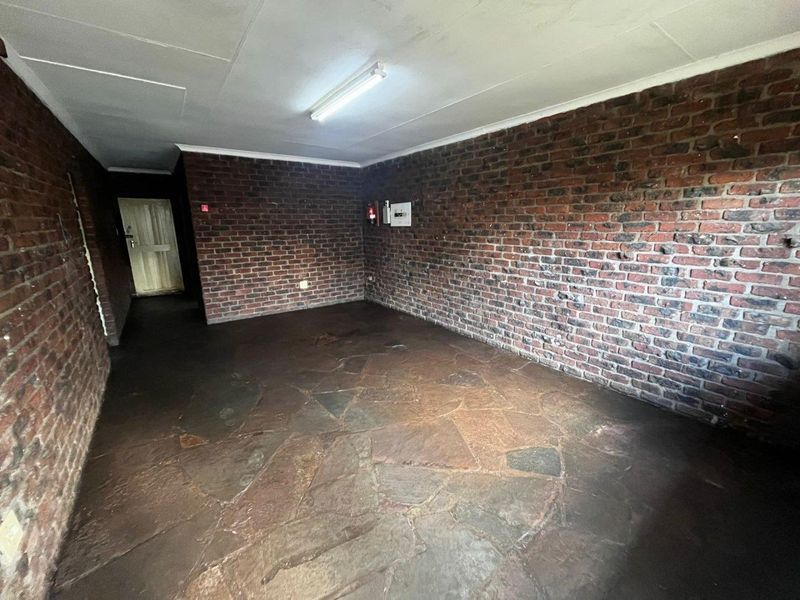 An empty living area featuring rustic exposed brick walls and traditional flagstone flooring, offering a blank canvas for renovation.