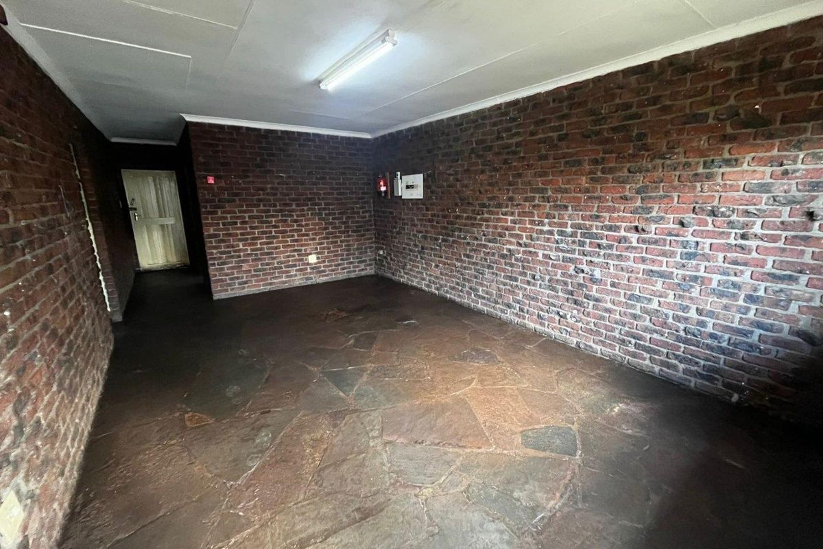 An empty living area featuring rustic exposed brick walls and traditional flagstone flooring, offering a blank canvas for renovation.