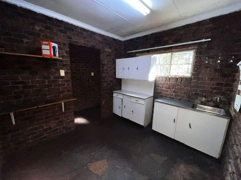 A basic kitchen area featuring exposed brick walls, built-in white cabinetry, and a stainless steel sink, offering significant potential for renovation and modernization.
