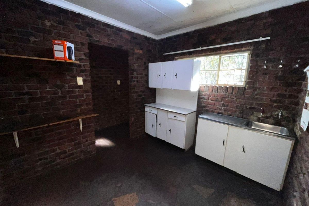A basic kitchen area featuring exposed brick walls, built-in white cabinetry, and a stainless steel sink, offering significant potential for renovation and modernization.