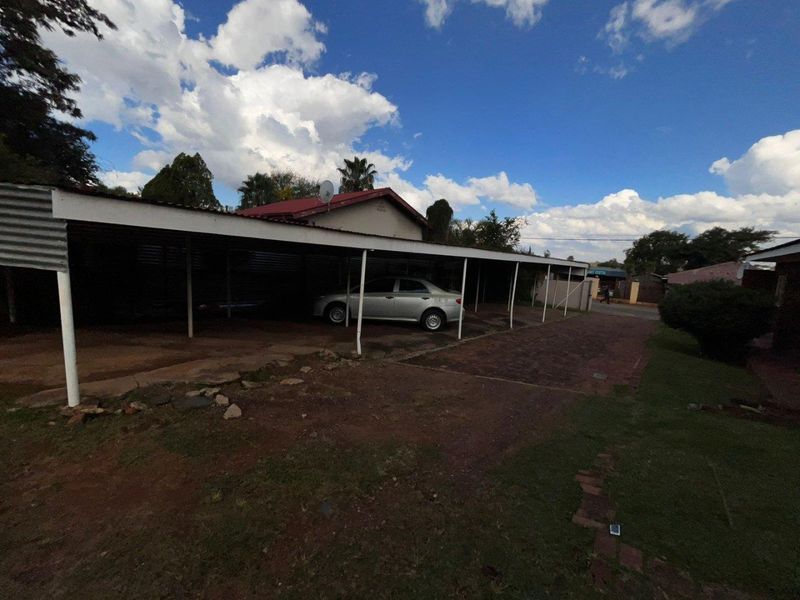 An outdoor carport structure providing covered parking space with a paved driveway and metal roofing.