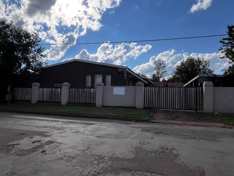 Front exterior view of the property featuring a secure brick perimeter wall, metal gate, and paved driveway access from the street.