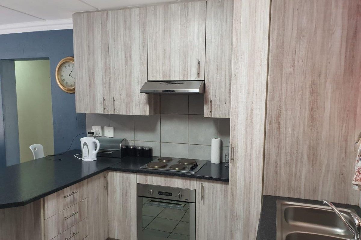 A functional kitchen featuring light wood-grain laminate cabinetry, dark countertops, a built-in oven with electric hob, and a stainless steel double sink.