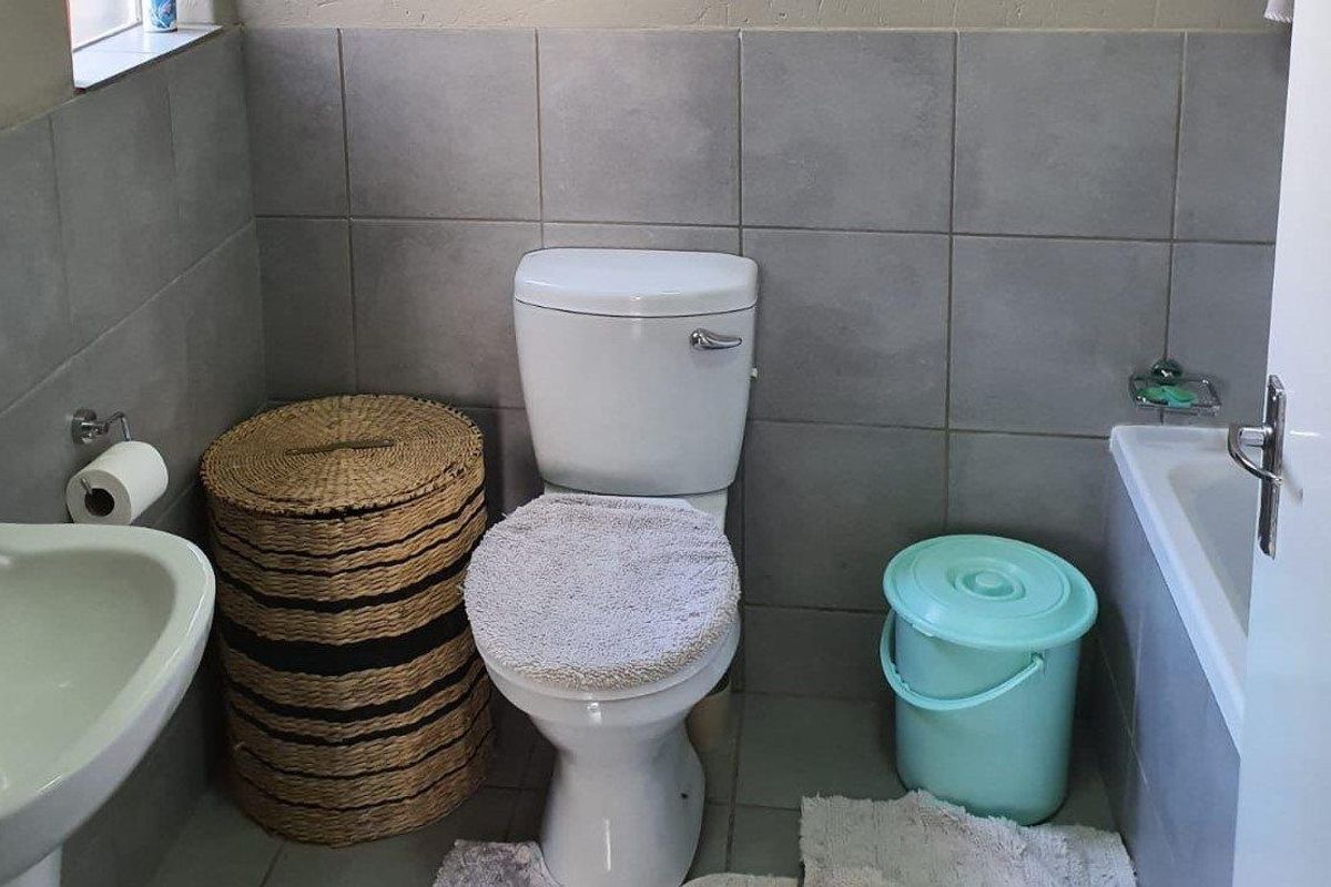 A functional bathroom featuring a bathtub, pedestal basin, and toilet, finished with neutral grey wall and floor tiling.