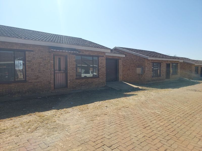 Front exterior view of a face brick townhouse complex featuring tiled roofs, paved driveway access, and secure entrance points.