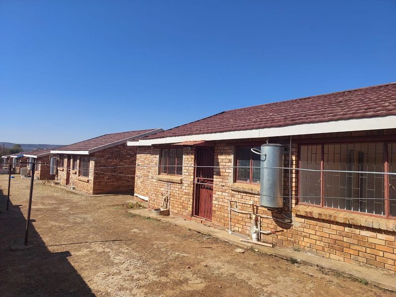 Rear view of a row of face brick townhouses featuring tiled roofs, security bars on windows, and external geyser installations.