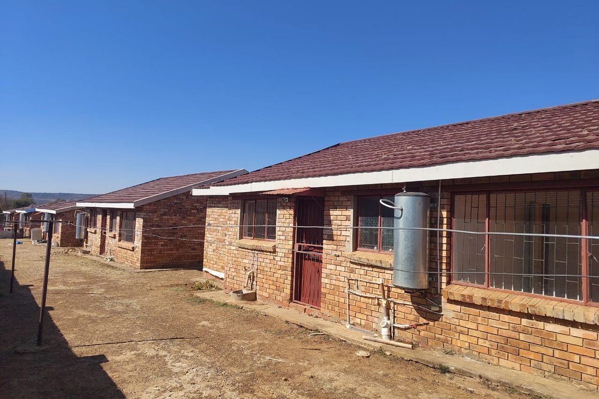 Rear view of a row of face brick townhouses featuring tiled roofs, security bars on windows, and external geyser installations.
