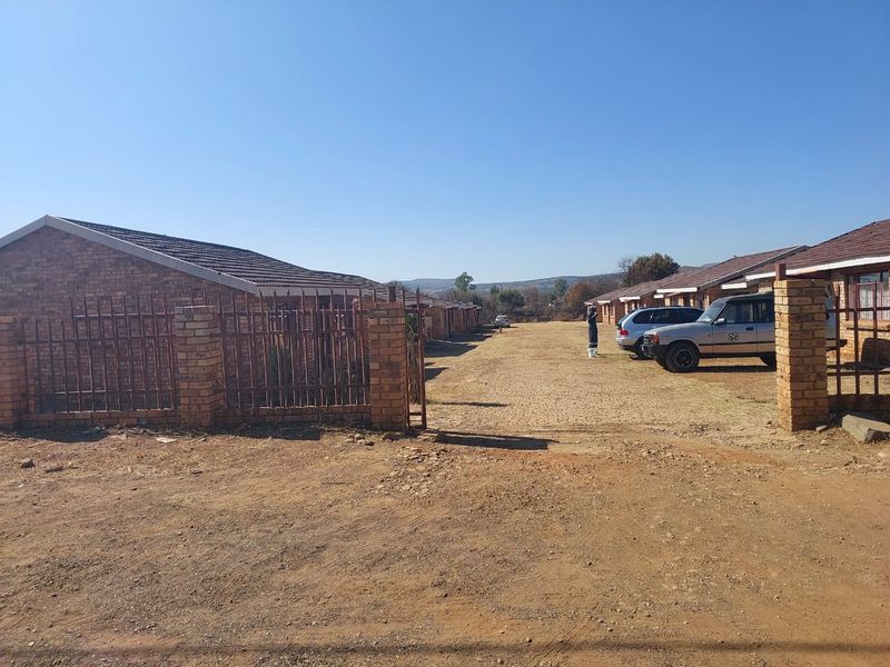 Exterior view of a townhouse complex featuring face brick construction, tiled roofs, and an unpaved driveway area.