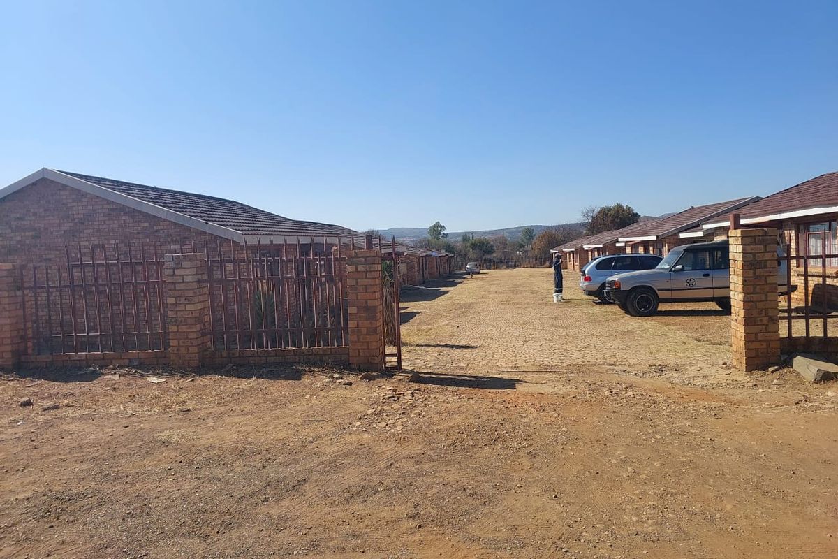Exterior view of a townhouse complex featuring face brick construction, tiled roofs, and an unpaved driveway area.