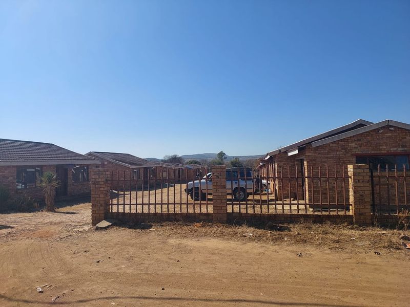 Exterior view of a townhouse complex featuring face brick construction, tiled roofing, and metal perimeter fencing with a gravel driveway.