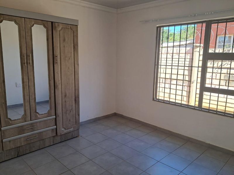 A bedroom featuring tiled flooring and a window fitted with security bars, providing a functional and secure living space.