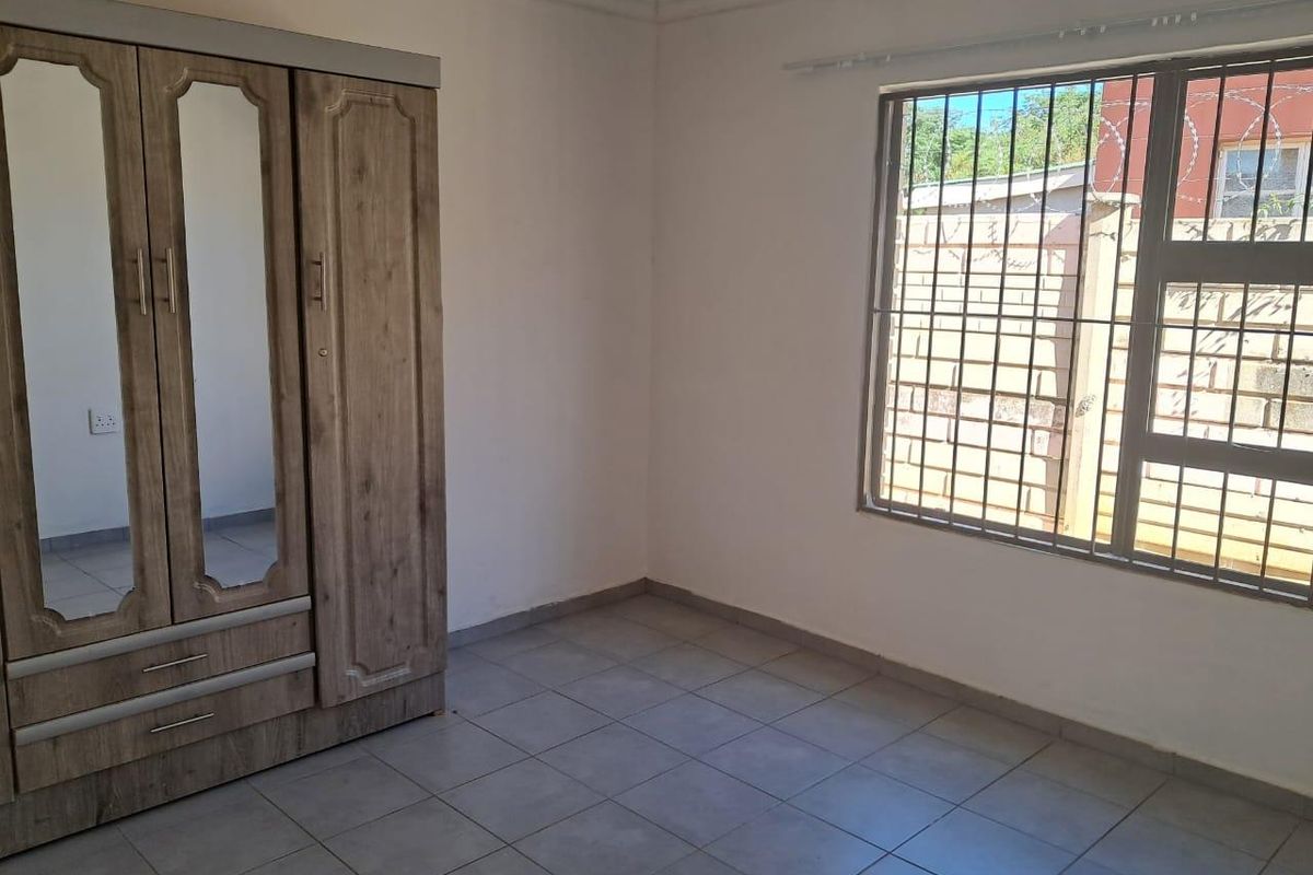 A bedroom featuring tiled flooring and a window fitted with security bars, providing a functional and secure living space.