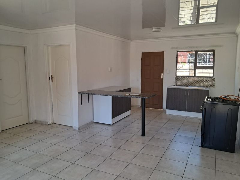 An open-plan kitchen area featuring tiled flooring, built-in cabinetry with a breakfast bar, and a stainless steel sink, presented in a clean, vacant state.