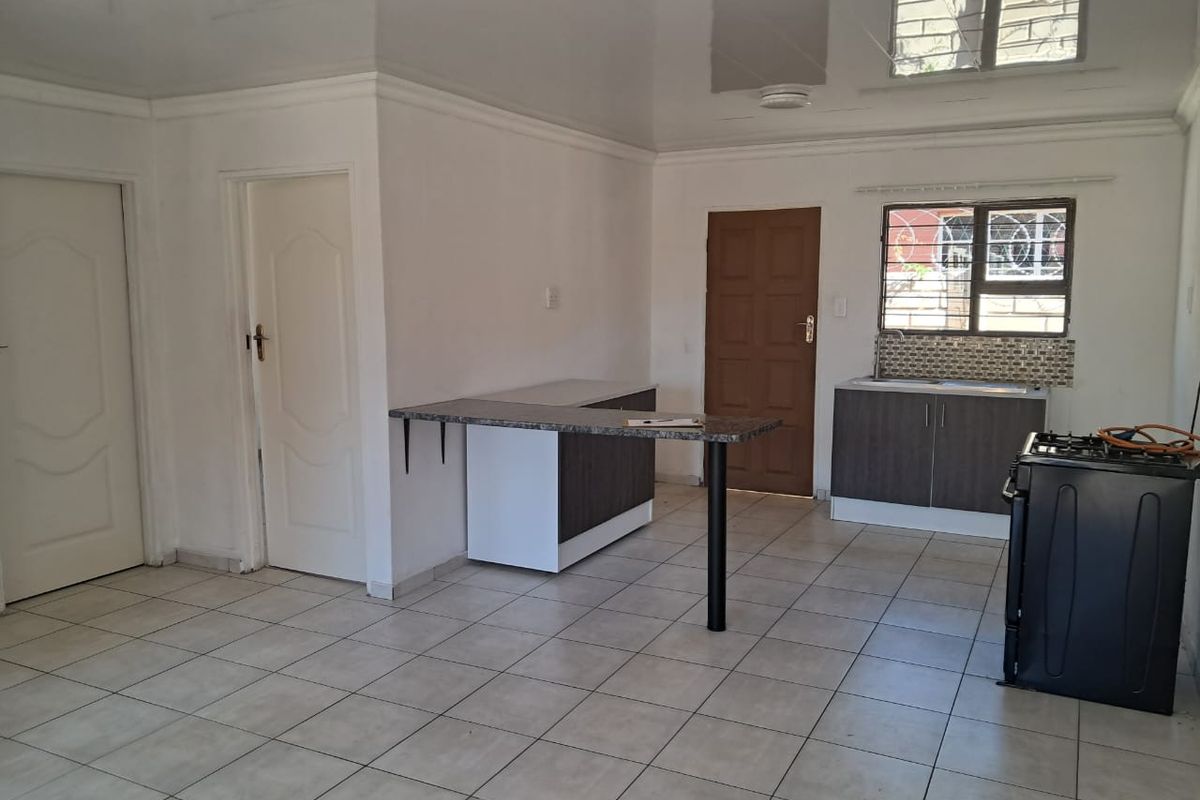 An open-plan kitchen area featuring tiled flooring, built-in cabinetry with a breakfast bar, and a stainless steel sink, presented in a clean, vacant state.