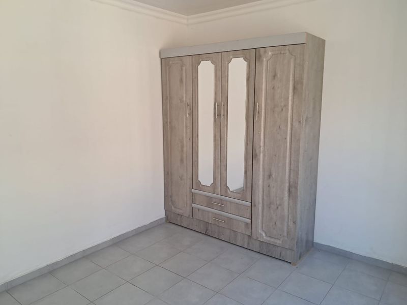 A simple bedroom featuring neutral tiled flooring and a built-in wardrobe with mirrored panels.