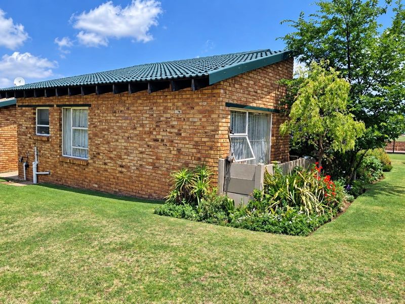 A view of the rear exterior of the townhouse featuring face brick construction, a tiled roof, and a well-maintained garden area.