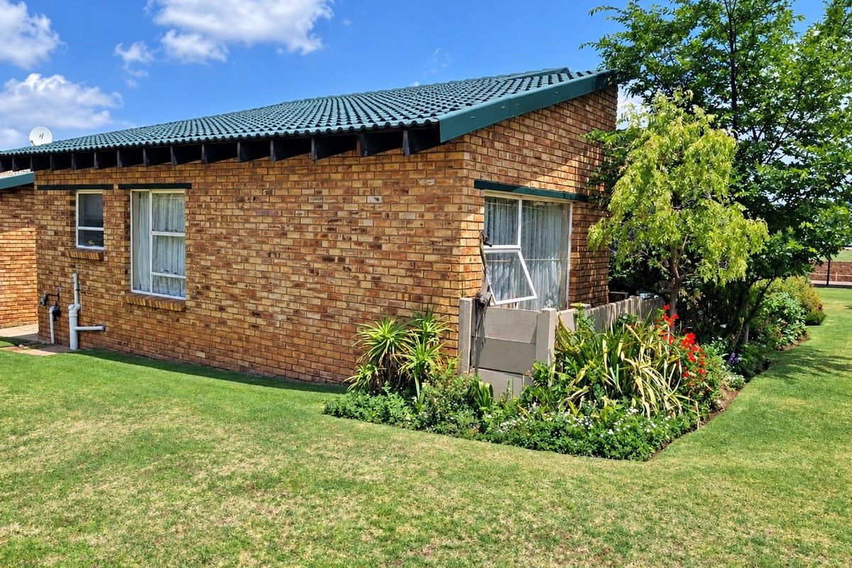 A view of the rear exterior of the townhouse featuring face brick construction, a tiled roof, and a well-maintained garden area.
