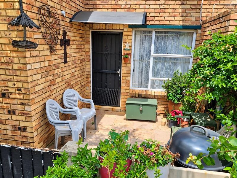 A private paved patio area featuring face-brick walls, a security gate, and a protective awning over the entrance.