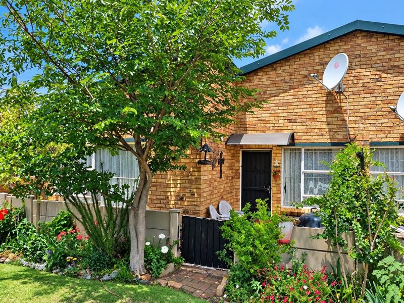 Front view of a face brick townhouse featuring a private garden, paved entrance path, security gate, and established landscaping.