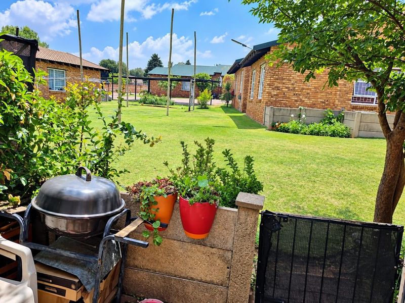 A view of the rear garden area featuring face brick townhouse exteriors, a well-maintained lawn, and a concrete boundary wall with a security gate.