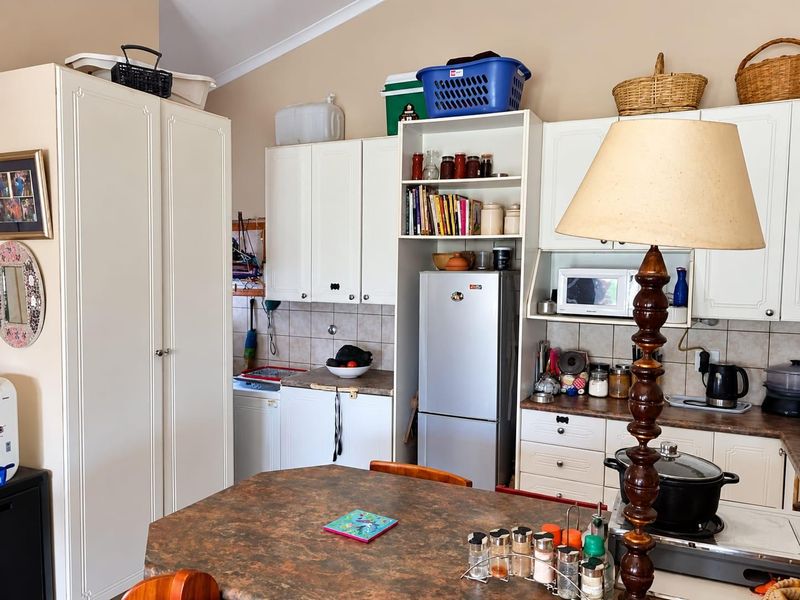 A functional kitchen featuring white cabinetry, tiled backsplash, laminate countertops, and a vaulted ceiling, providing a practical layout for daily meal preparation.